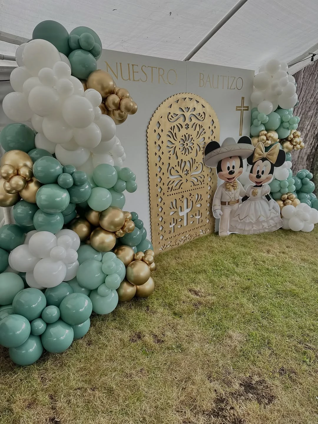 White, sage green and gold balloon garland framing a Nuestro Bautizo backdrop