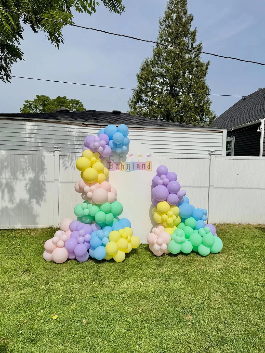 Pastel rainbow balloon garlands and an arched backdrop at an outdoor celebration